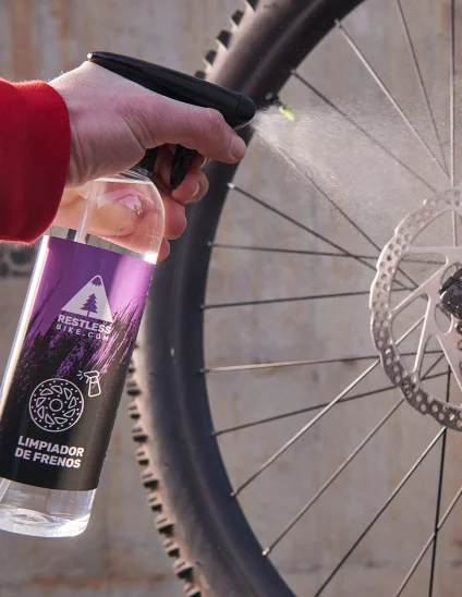 Mano aplicando spray limpia frenos directamente sobre el disco de una bicicleta de mtb